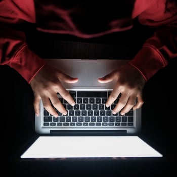 persoon achter laptop in een donkere kamer.